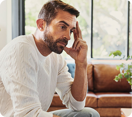 Man in a white sweater sitting on a couch having an anxious moment. He is feeling stressed and restless.